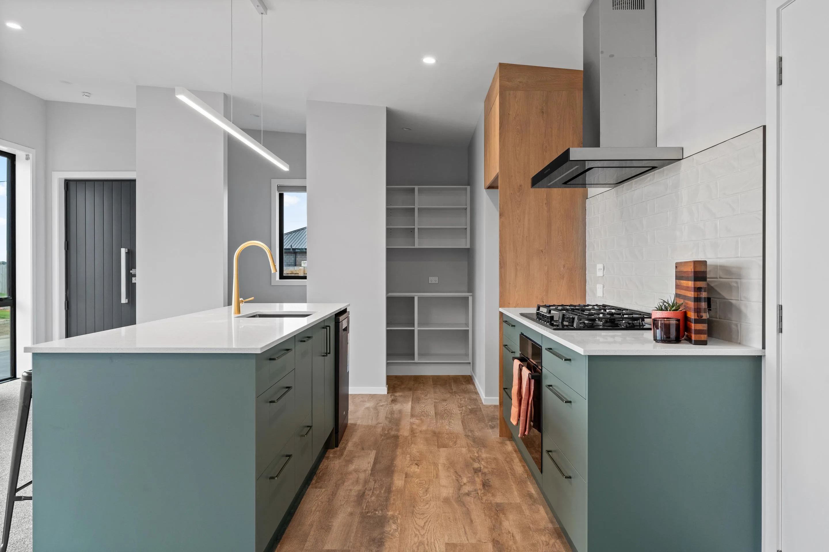 Completed Ember House kitchen with green cabinetry, timber flooring, and brass tapware